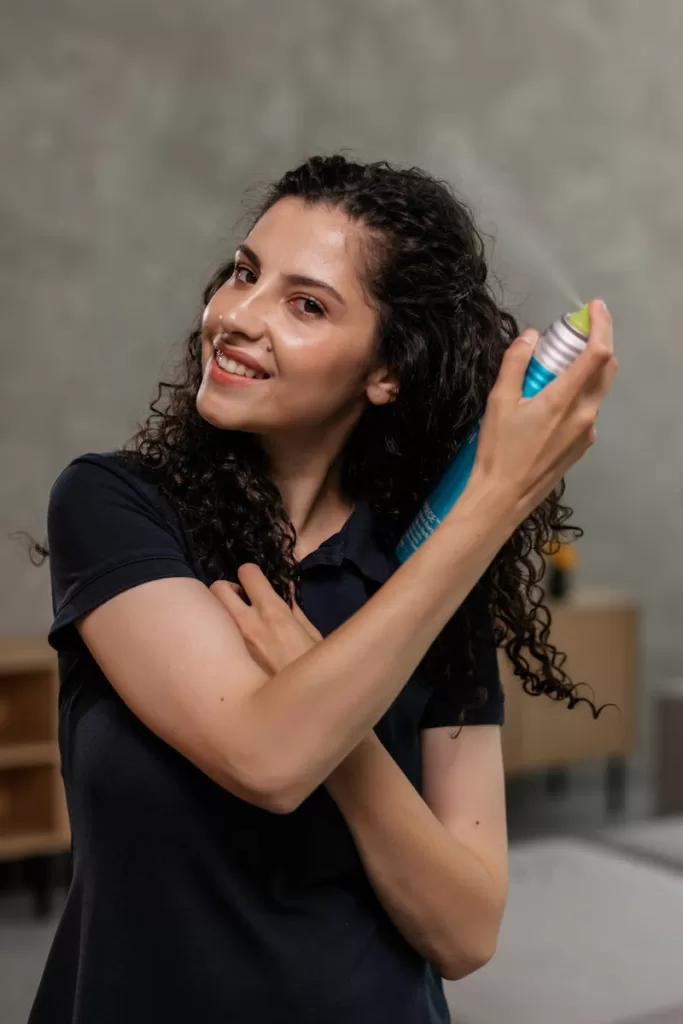 Fighting Frizz and Heat: Finding The Best Heat Protection Hair Spray in India Smiling woman using hair spray in a bright indoor setting. Ideal for beauty and personal care themes.
