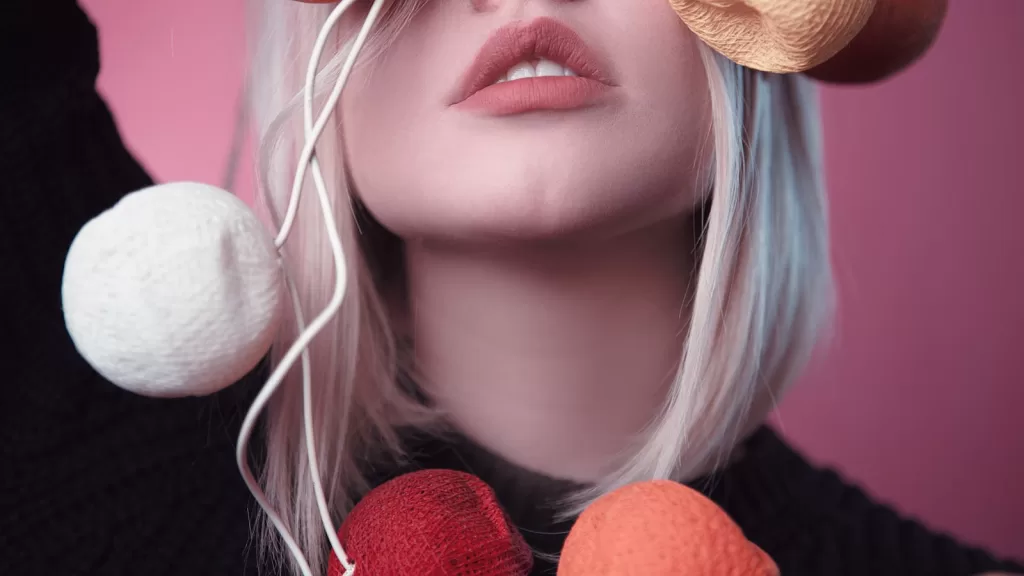 Finding the Best Lip Plumping Device in India: A Buyer's Guide Artistic close-up portrait of a stylish woman with colorful yarn balls on a pink background.