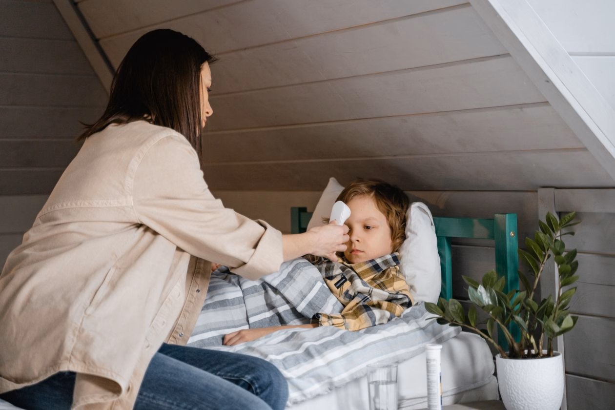Mother checking the temperature of a sick child lying in bed in a cosy bedroom, thermometer in hand, a typical fever-night scene