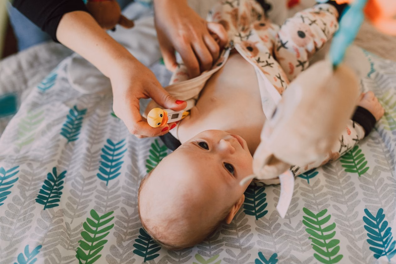 Best baby thermometer in India: parent using a digital thermometer to check a baby lying on a patterned bedspread at home
